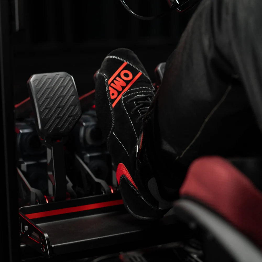 Simagic P-Active pedal face under a driver's racing boot, close-up in a sim racing cockpit